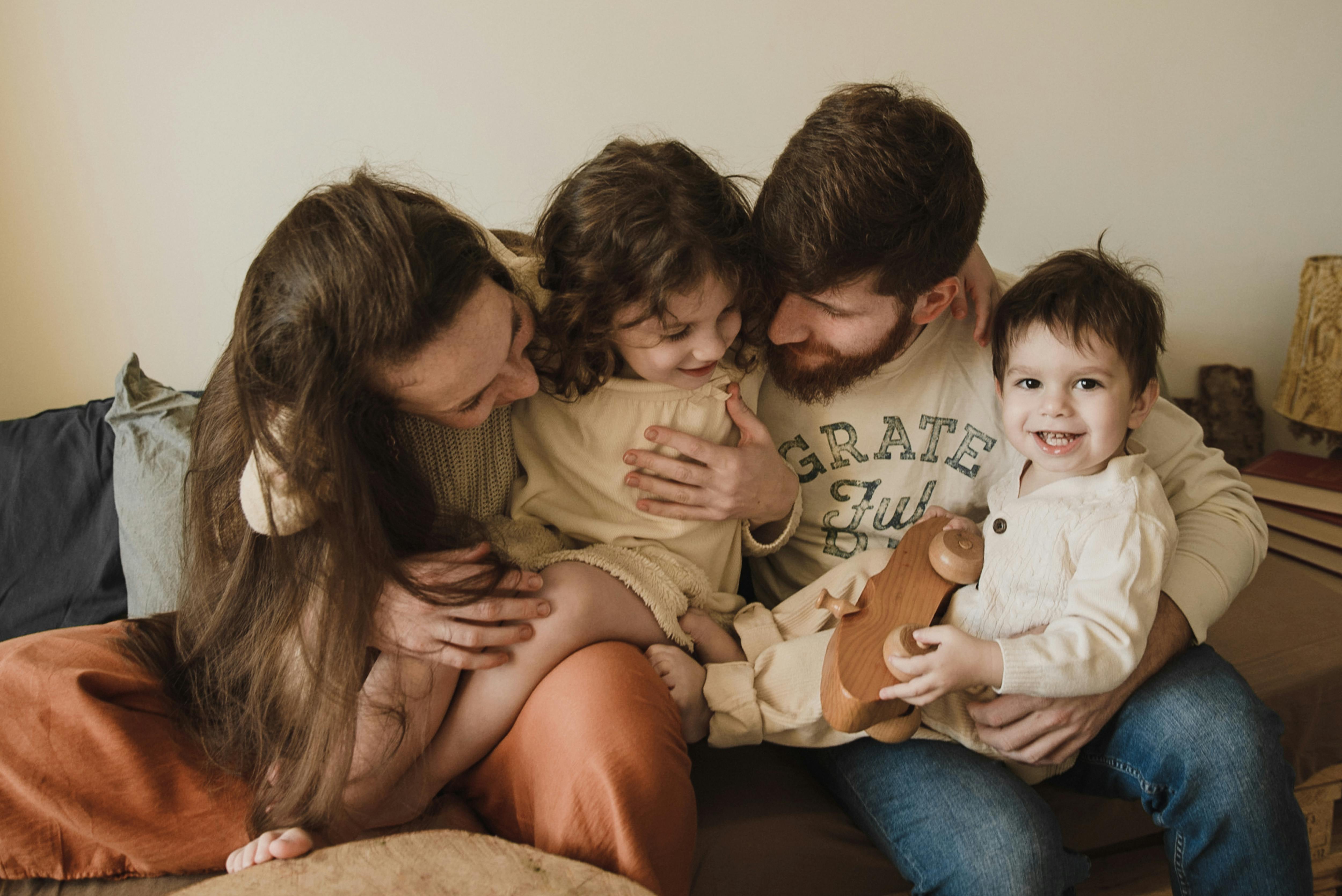 親密的家庭時光，父母與兩個小孩在客廳溫馨擁抱。