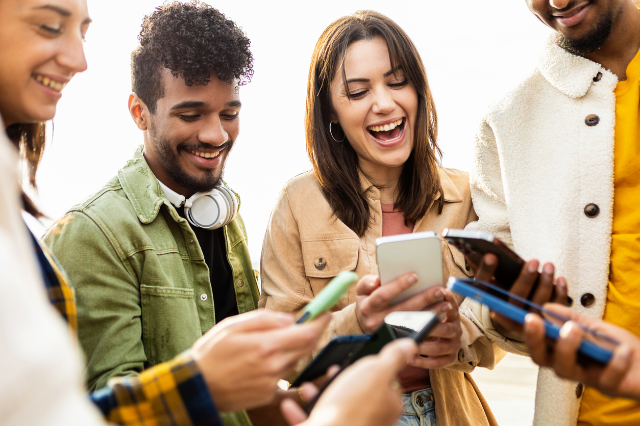 Happy group of young friends using smartphone in the street